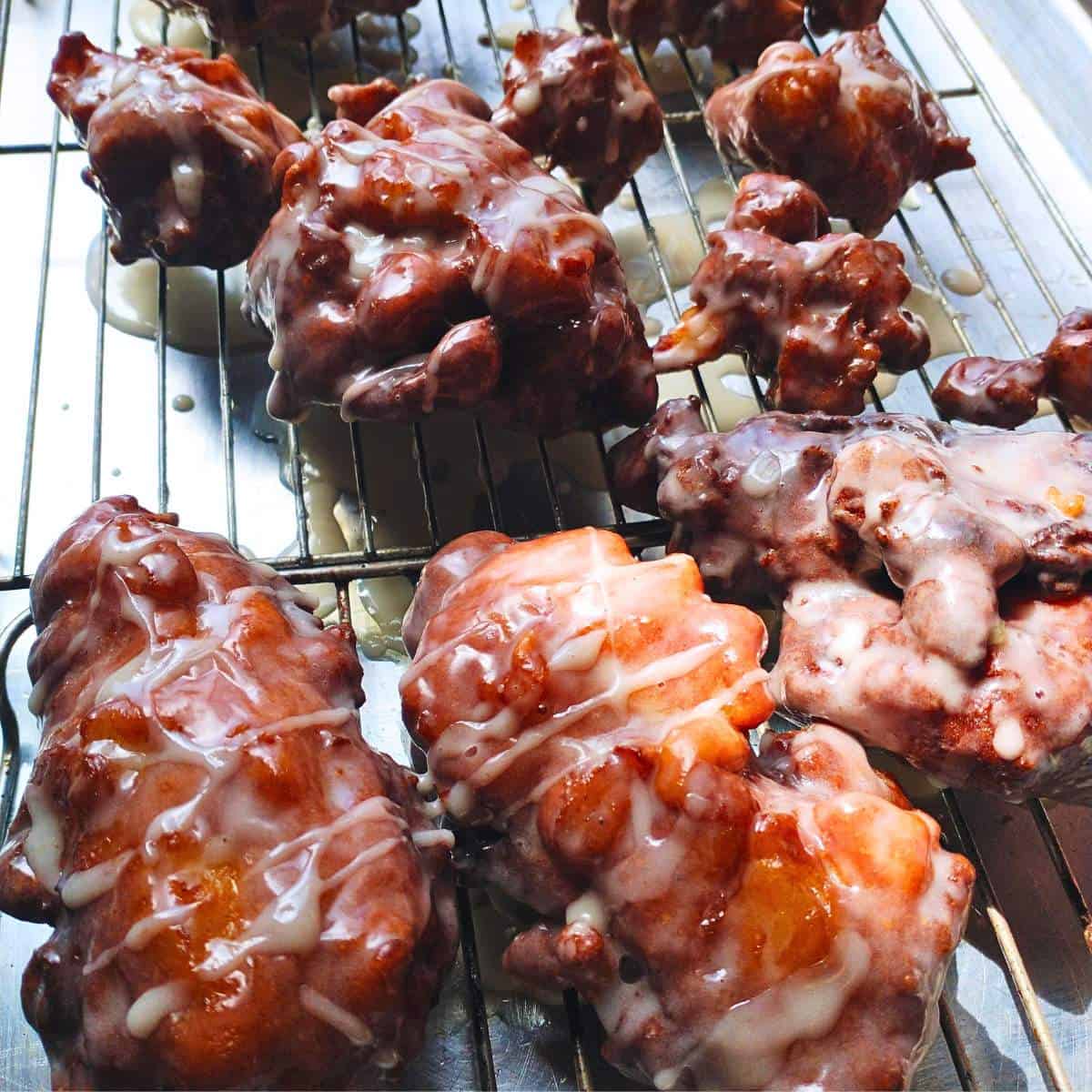 fried apple fritters on a metal baker's rack over a cookie sheet, dripping with fresh vanilla glaze.