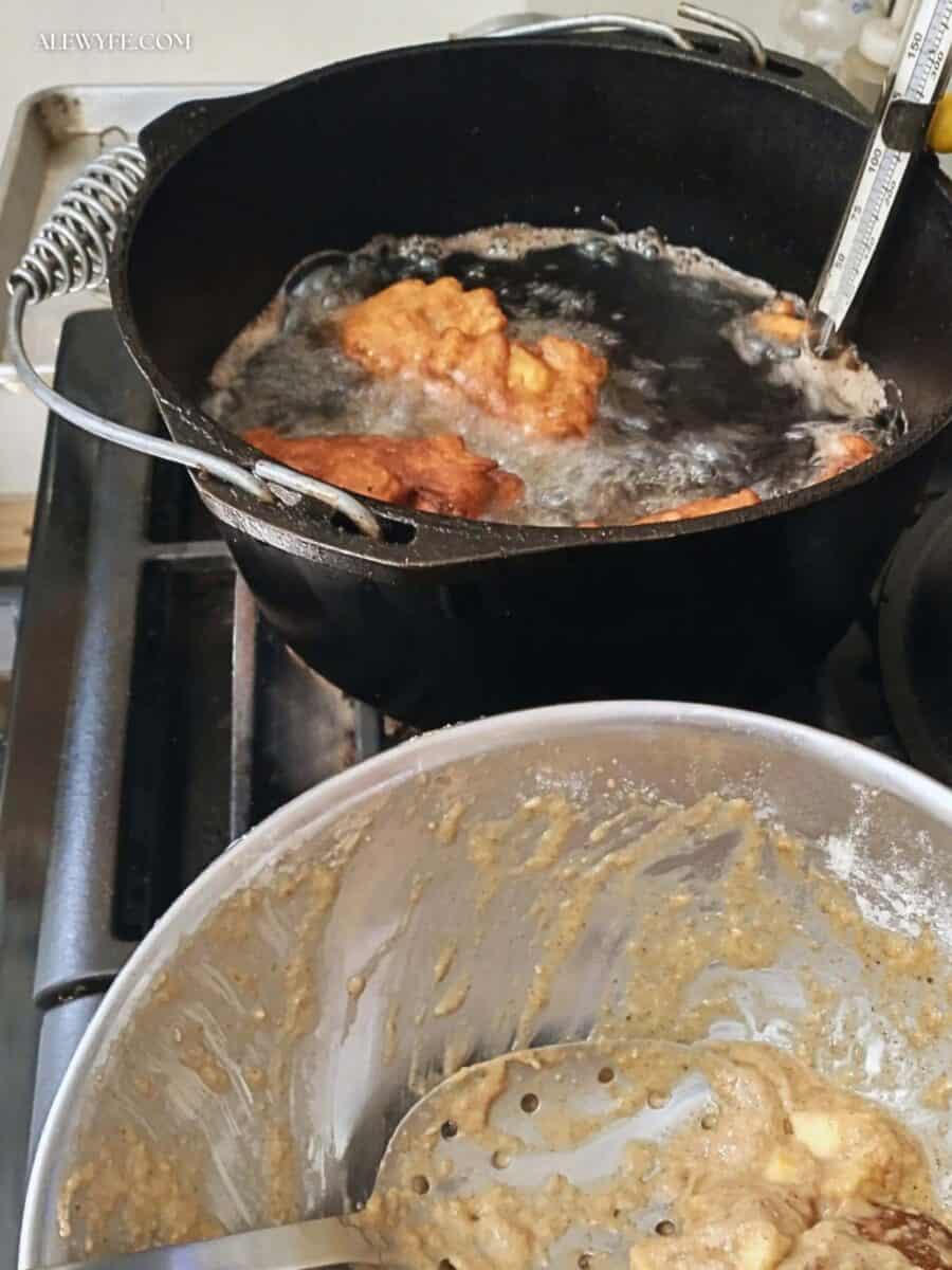 apple fritters frying in a pot of hot oil in the background, and a bowl of fritter batter in the foreground.