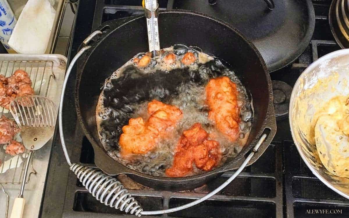 a stovetop with a pot of hot oil and frying apple fritters