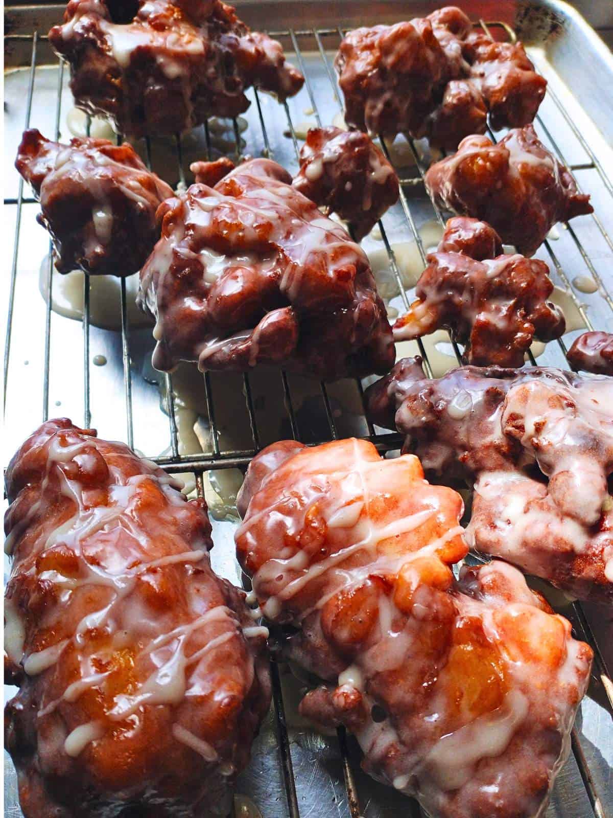 fresh fritters drizzled with vanilla glaze dripping over a sheet pan.