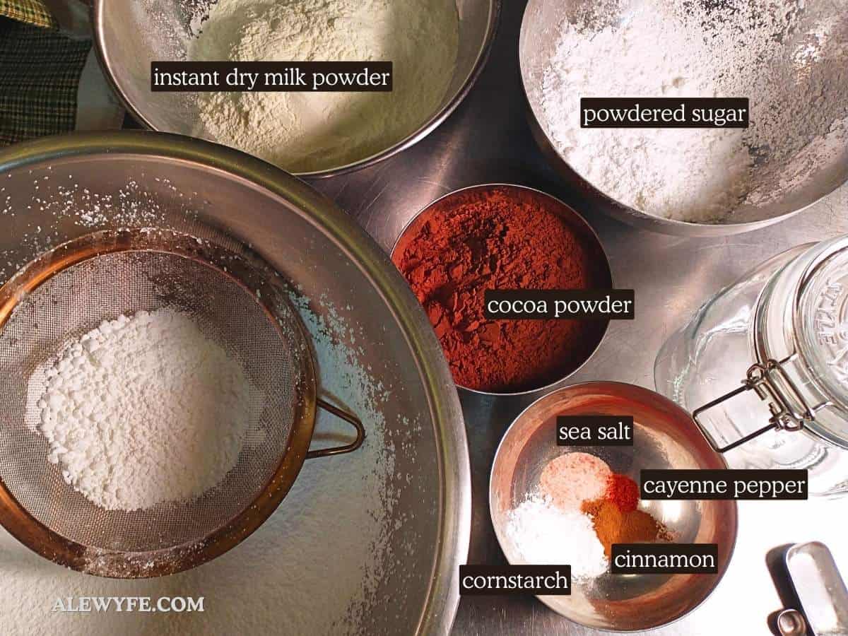 labeled photo with homemade hot chocolate mix ingredients (instant dry milk powder, powdered sugar, cocoa powder, sea salt, cayenne, cinnamon, cornstarch)