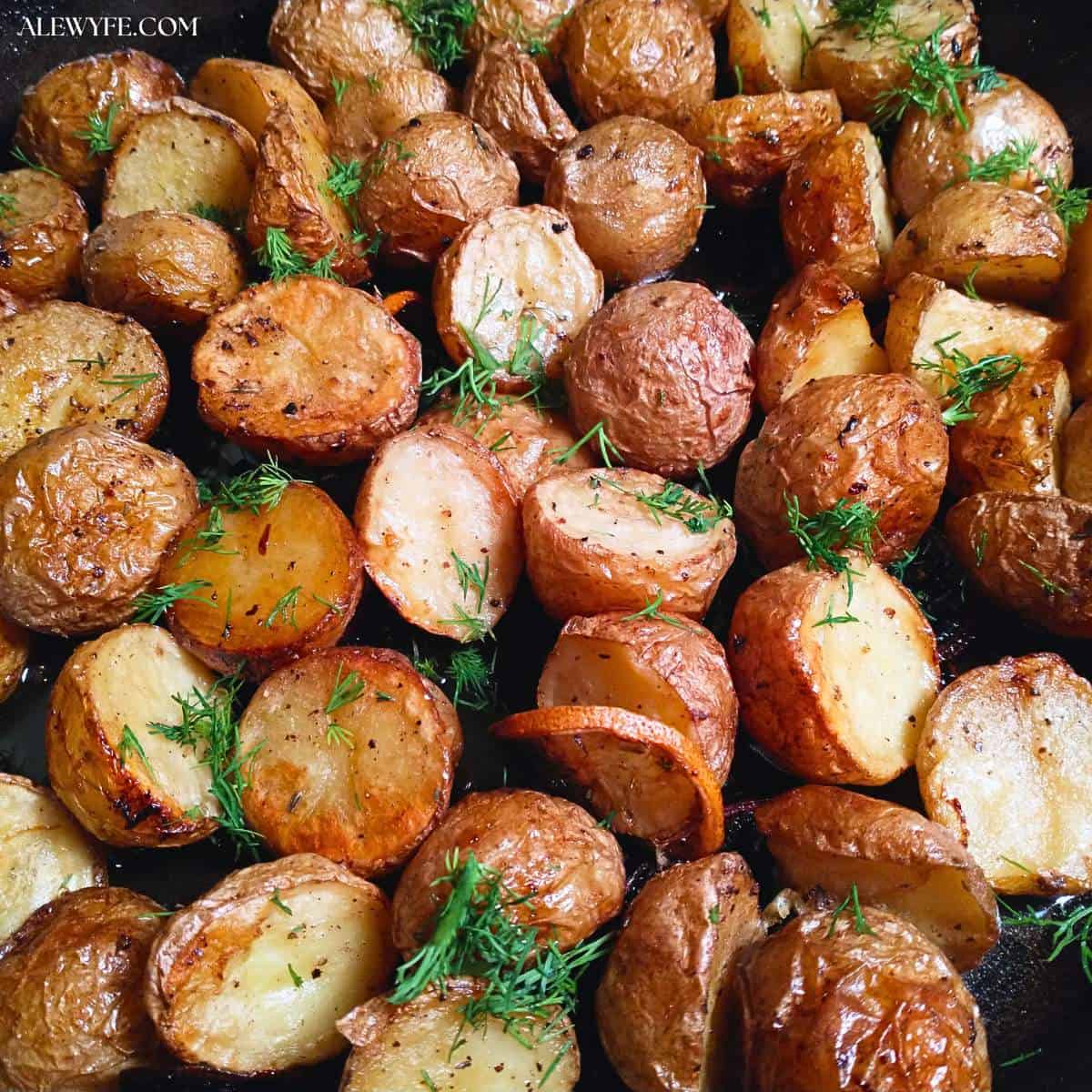 golden brown roasted potatoes with fresh dill and lemon slices in a cast iron pan