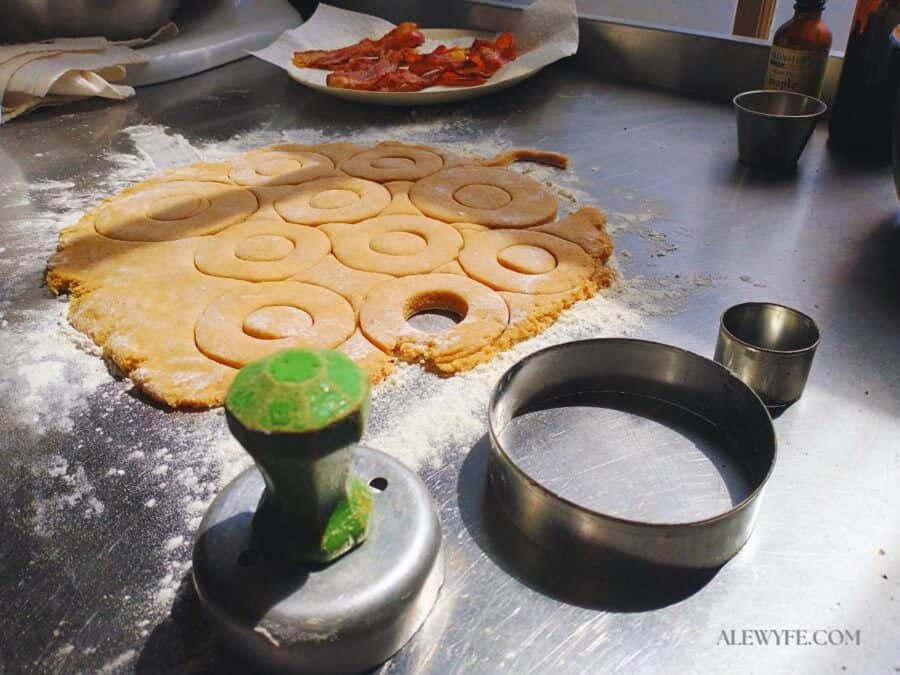 doughnut dough rolled out on a floured stainless counter, with an assortment of circle cutters