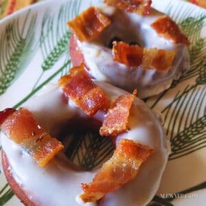 side angle photo of two glazed maple bacon protein doughnuts, topped with pieces of crispy bacon and glaze