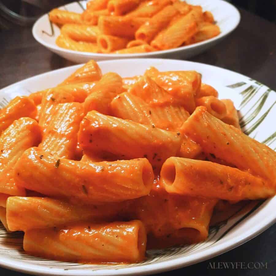 two bowls of rigatoni pasta tossed with roasted red pepper cream sauce