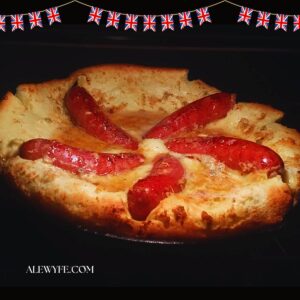toad in the hole sausage pudding baking in a skillet against a black background with union jack border