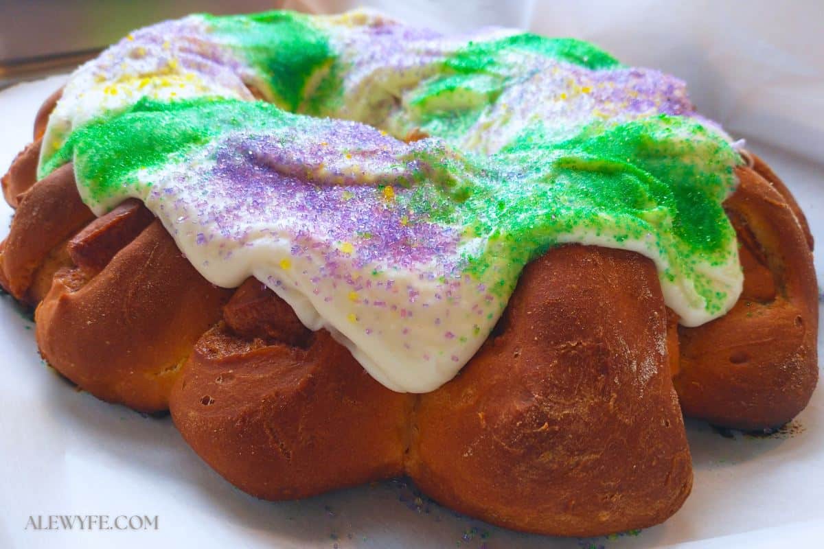 close up view of a king cake with cream cheese frosting and colorful sugar decoration.