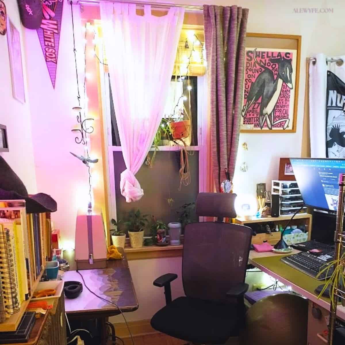 a brightly colored workspace with pink and white mood lighting at night. a computer desk is on the right and a sewing and craft table on the left, along with books on a shelf.