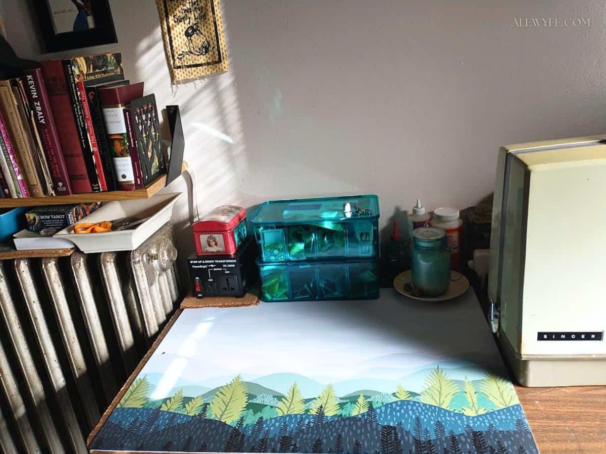 a craft cutting mat with a colorful woodland print is on a sewing table, along with bins and tins of thread, sewing notions, and craft supplies.