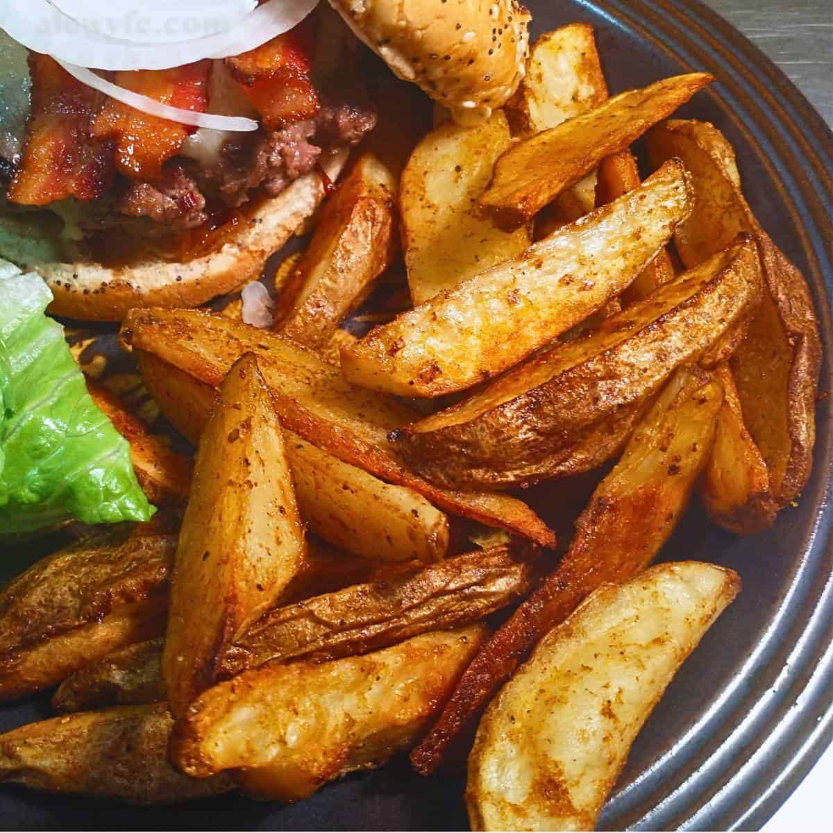 a plate overflowing with cajun crispy potato wedges along with a bacon cheeseburger.