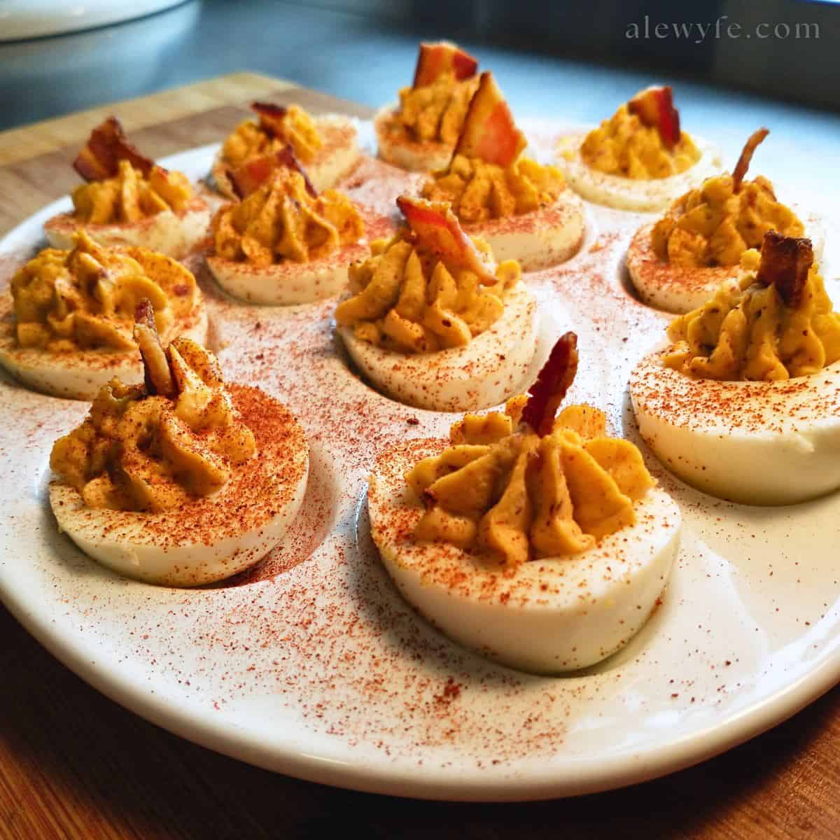 a platter of deviled eggs, with a dusting of paprika over the top and a bacon garnish in each egg.