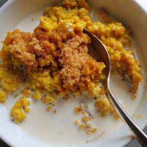 a bowl of turmeric-tinted golden oats with a silver spoon, milk, and brown sugar.