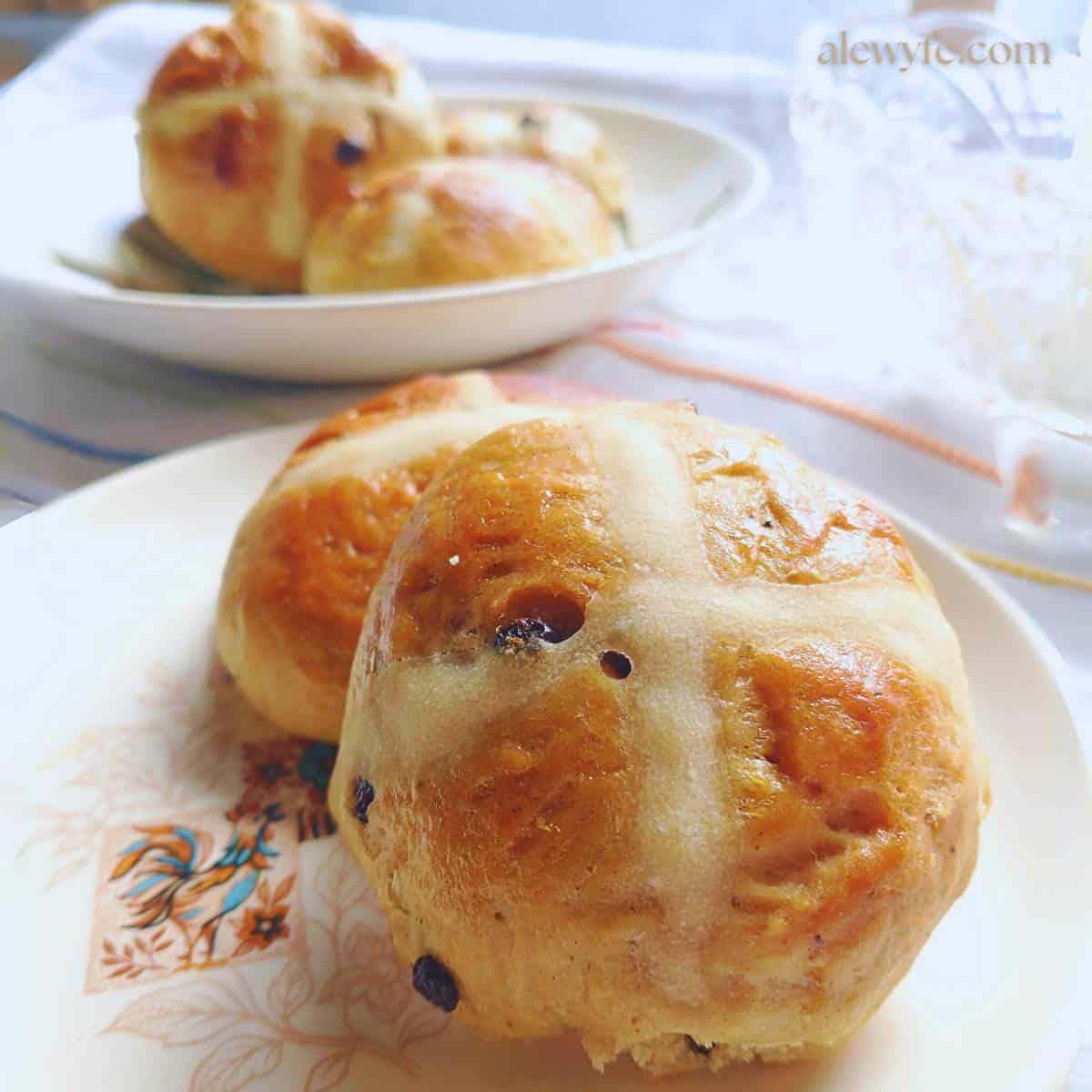 side view of two plates of traditional hot cross buns with currants, on a vintage plate with a crowing rooster.