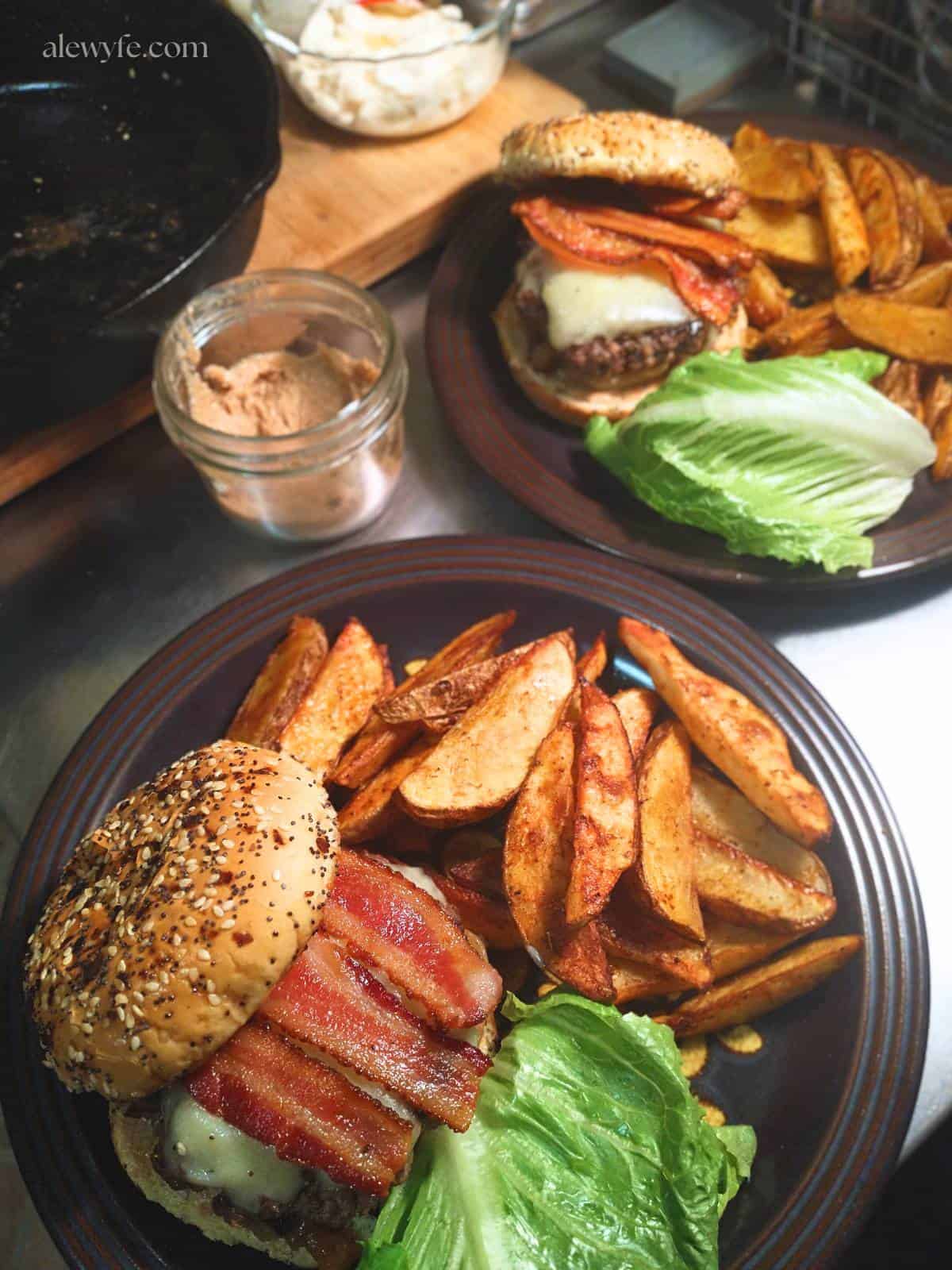 two plates of cajun crispy potato wedges with venison bacon cheeseburgers.