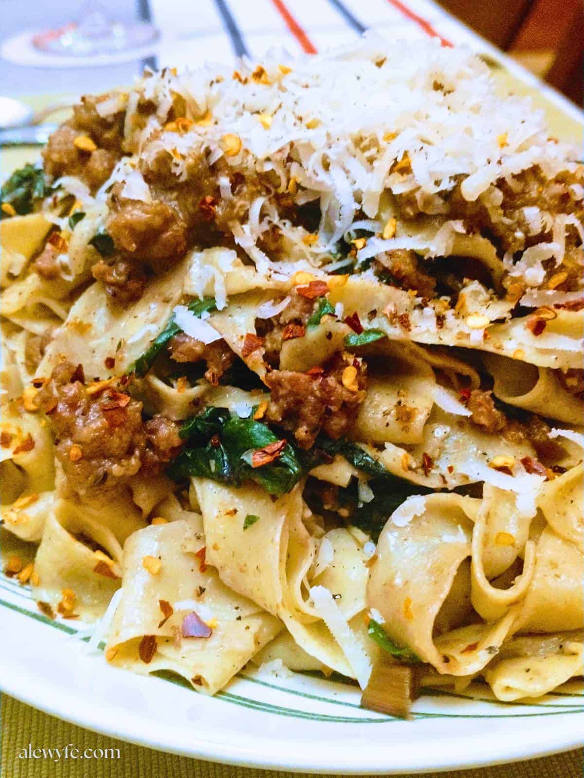 a bowl of homemade whole wheat pappardelle pasta noodles topped with pork ragu, swiss chard greens, red pepper flakes, and grated Parmesan cheese