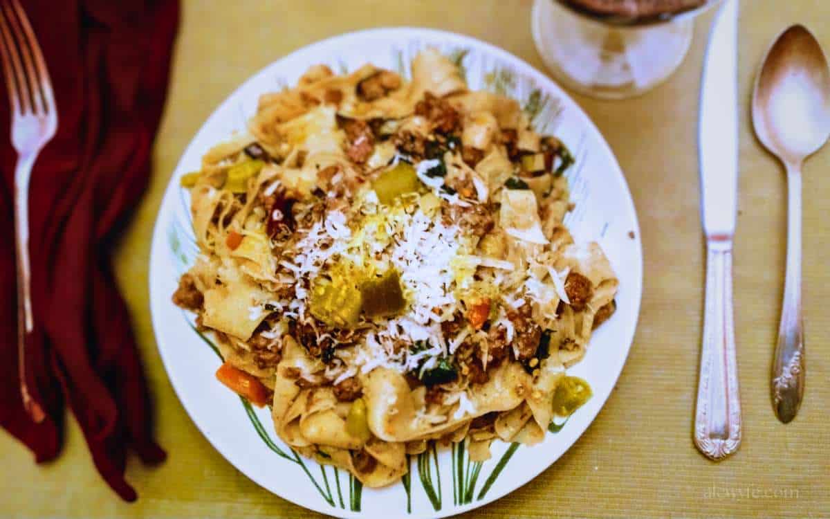 top down plate shot of a table setting with a bowl of whole wheat pappardalle with pork ragu, cheese, and giardianera.