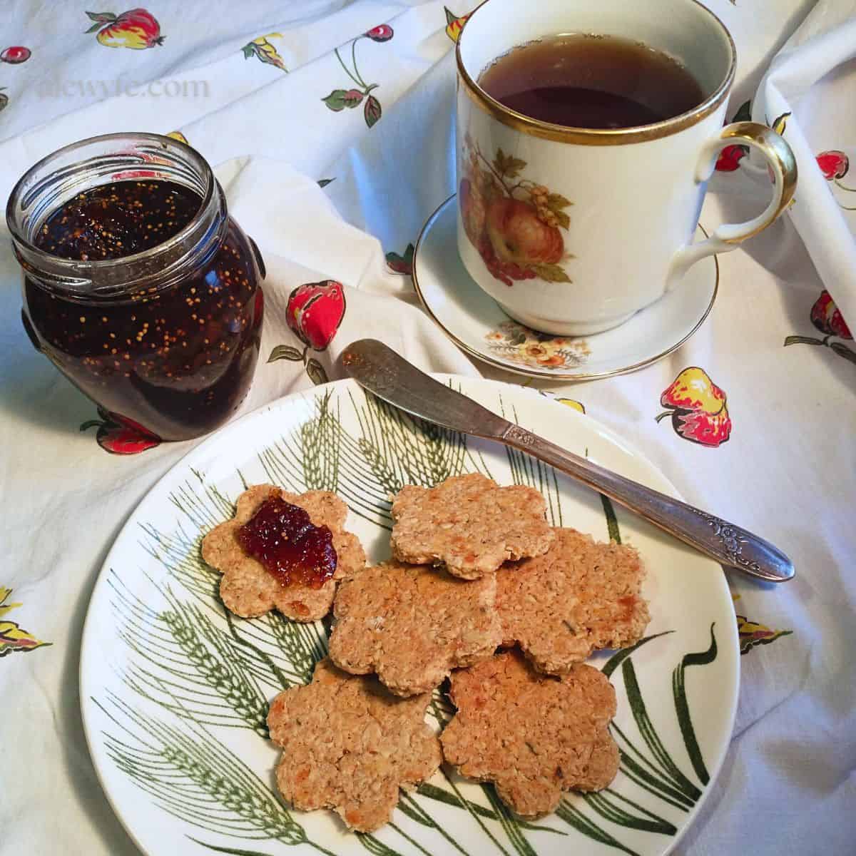 a plate of flower-shaped herb & cheese oatcakes with fig jam and a mug of tea.