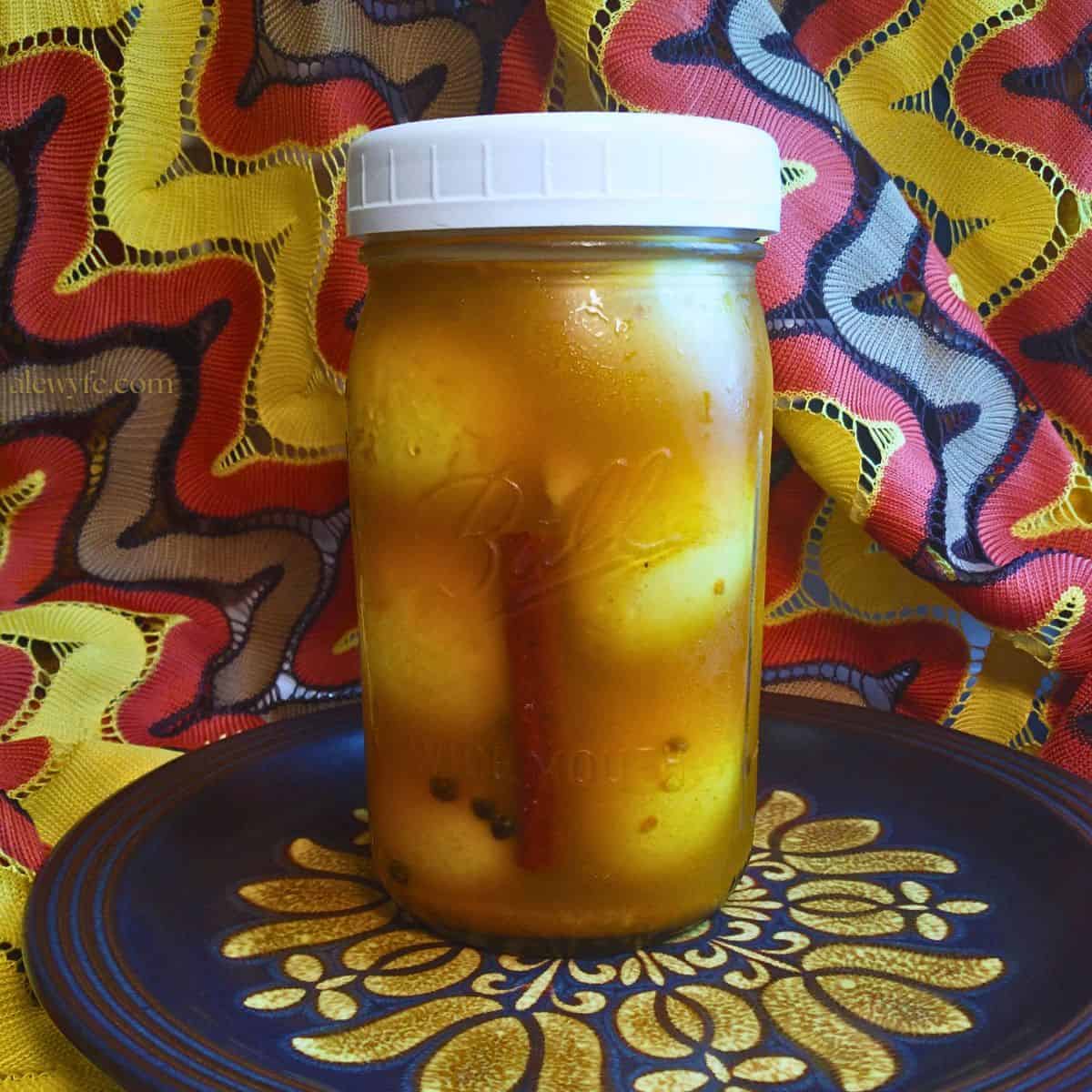 a quart jar of spiced golden pickled eggs on a plate in front of a vintage lace background with an orange, brown, and yellow pattern.