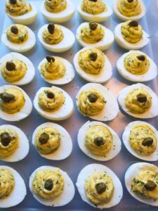 a tray of homemade lemon dill deviled eggs, each garnished with a large caper and a sprinkle of fresh dill and ready to serve.
