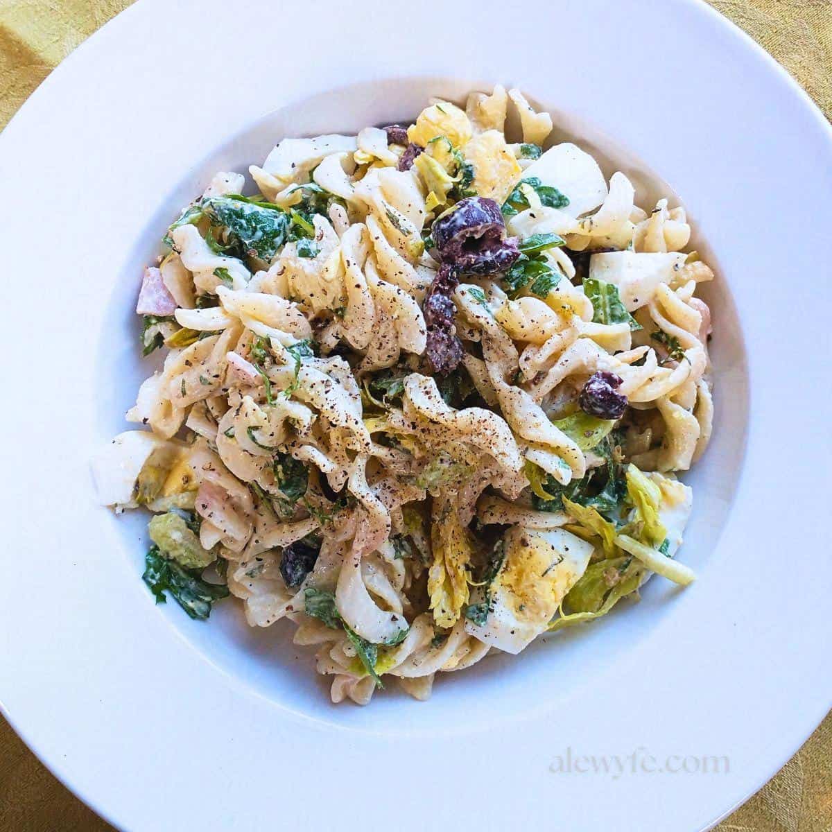 top down view of a bowl of arugula olive pasta salad with a creamy dressing.
