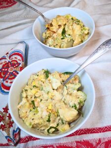 two bowls of old fashioned southern potato salad on a red and white tablecloth, with a brightly printed paisley cloth napkin.
