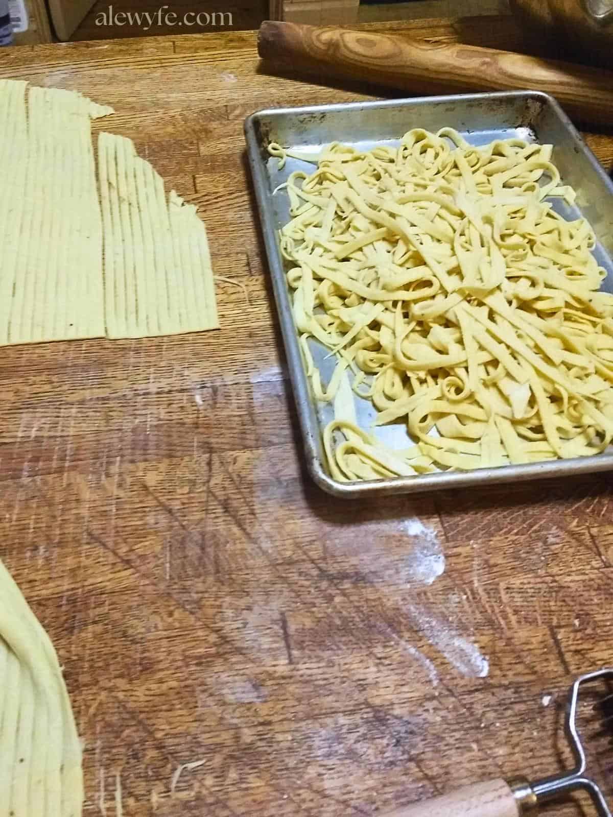 a tray of freshly cut fettuccine pasta with more rolled out and just cut pasta. 