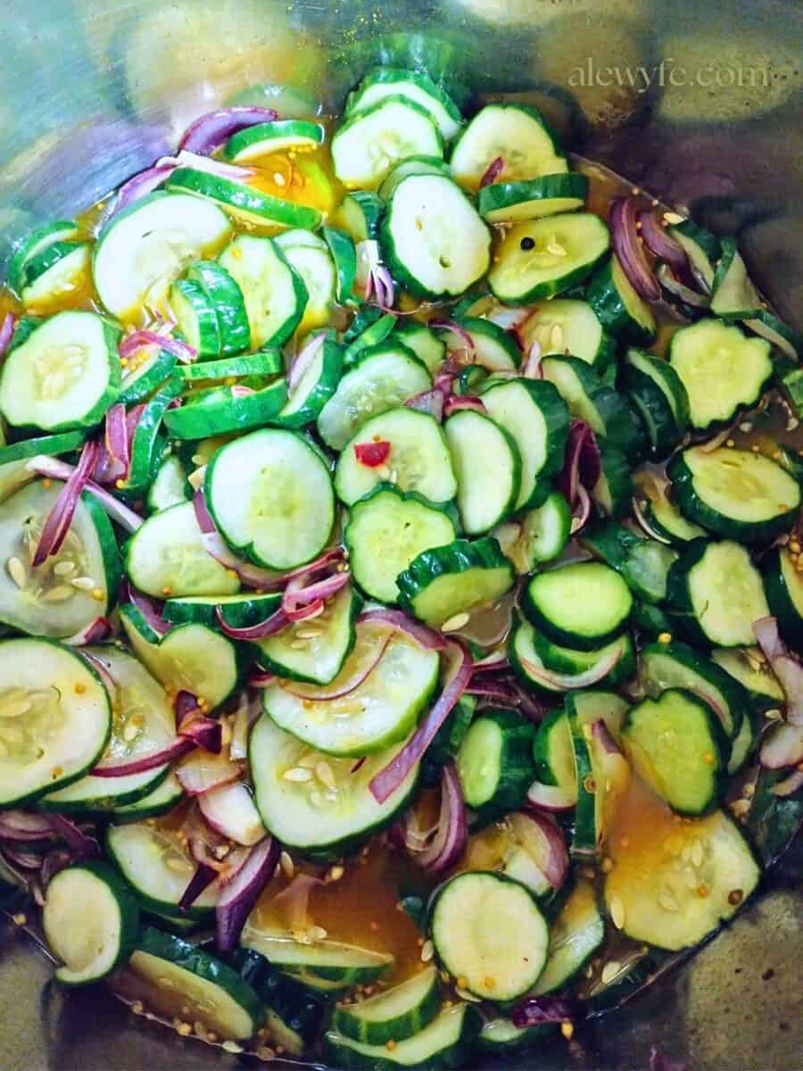 a pot of sliced cucumbers and red onions in spiced turmeric yellow pickling brine with whole spices.