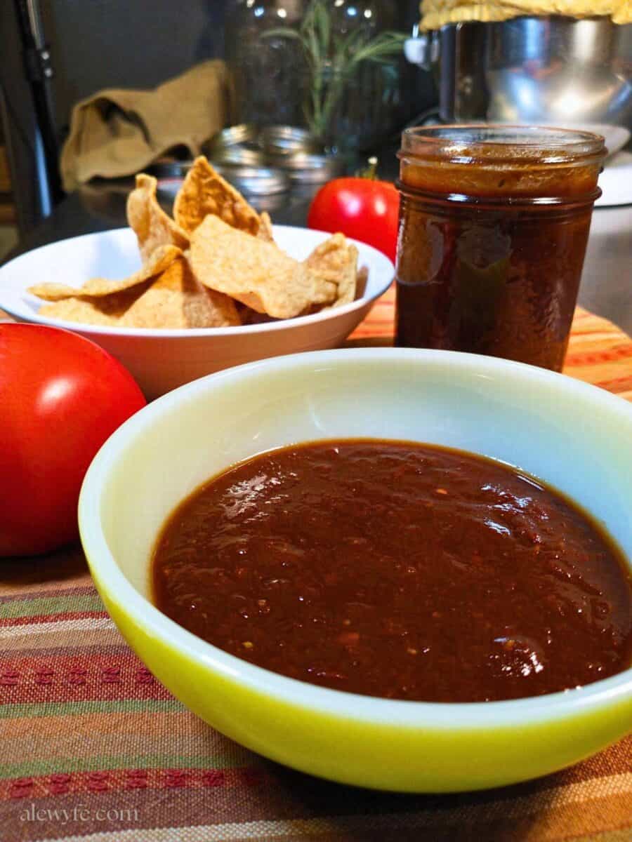 a small dipping bowl of salsa roja with a bowl of tortilla chips and a jar of salsa.