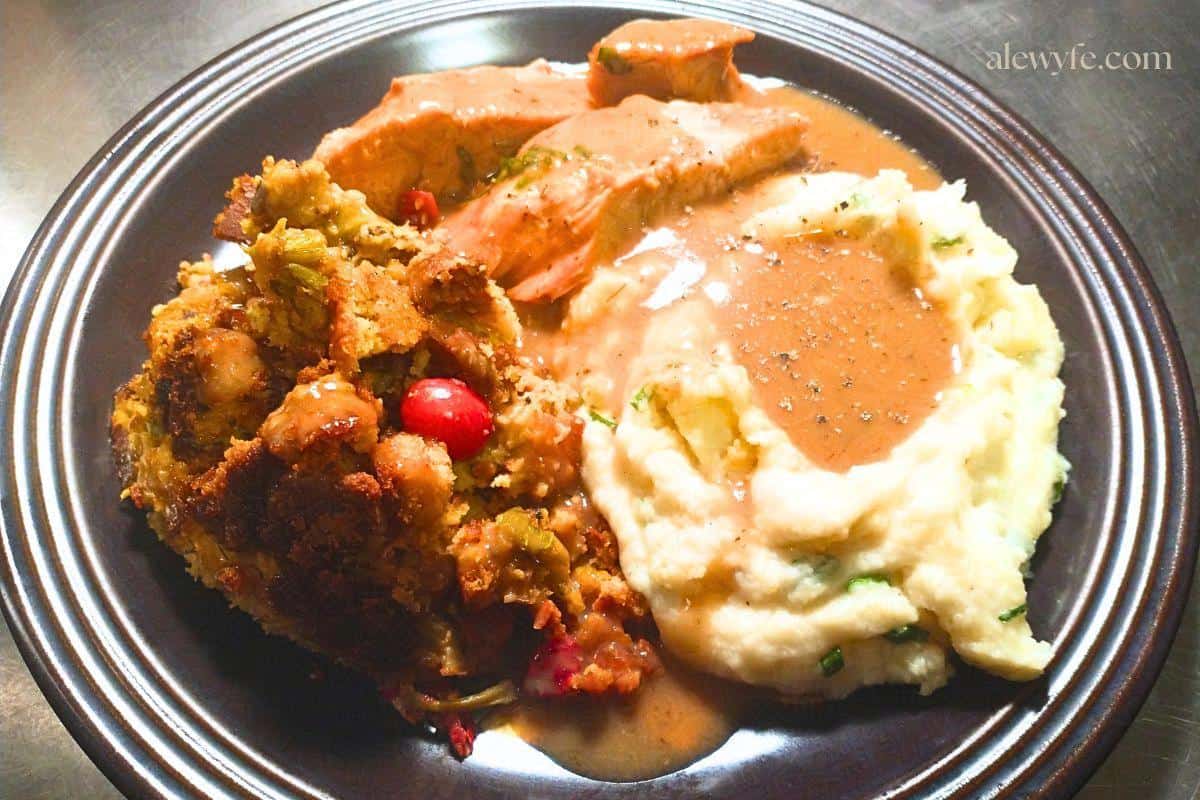 a plate with sliced turkey, mashed potatoes and gravy with cranberry cornbread dressing. 