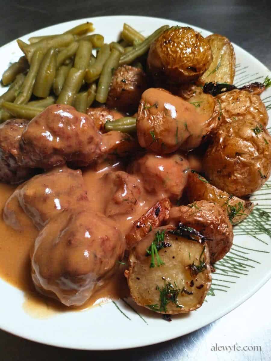 a plate of swedish meatballs with roasted potatoes, green beans, & gravy.