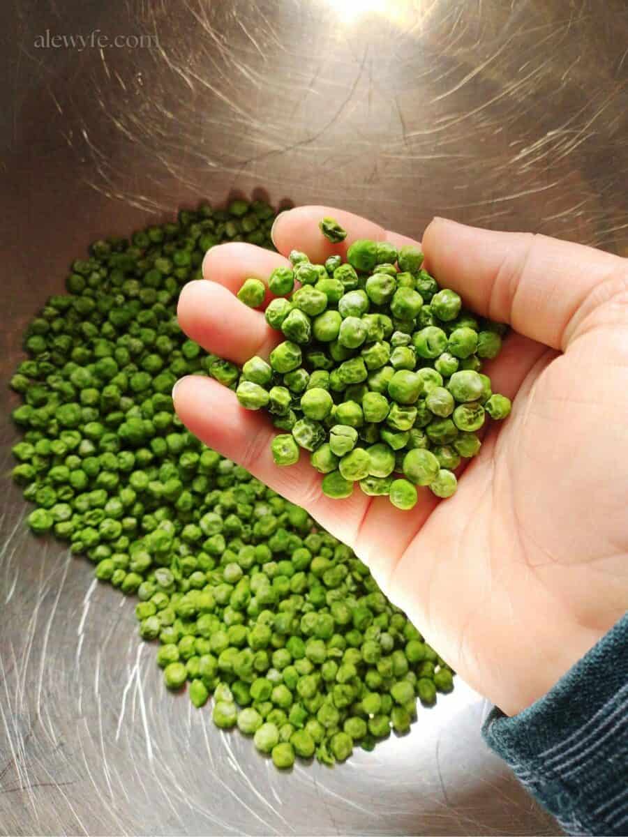 a handful of bright green dried peas with a bowl full of them in the background. 