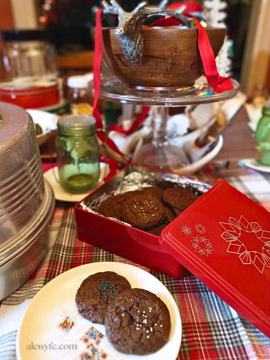 a small plate of molasses cookies in front of a cookie tin on a festive holiday table.