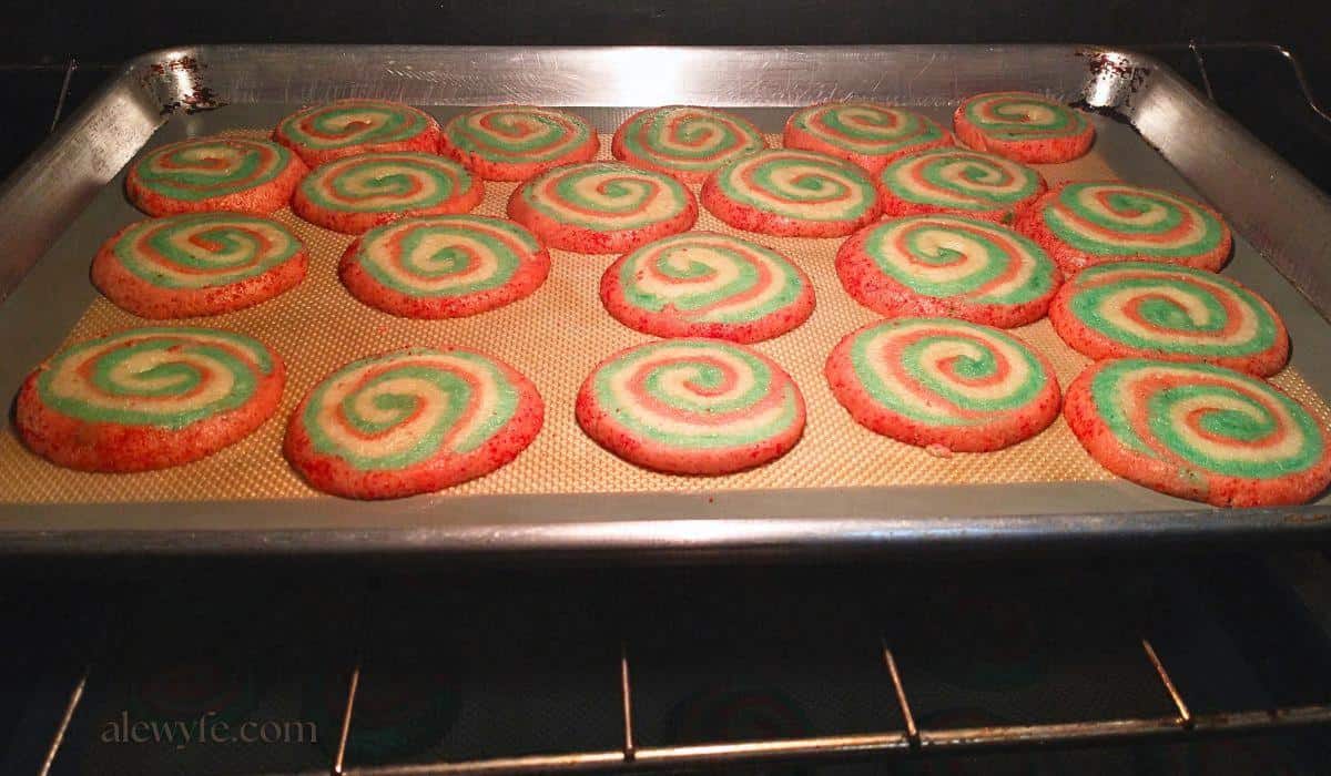 red, green, and white pinwheel spiral cookies baking on a cookie sheet. 