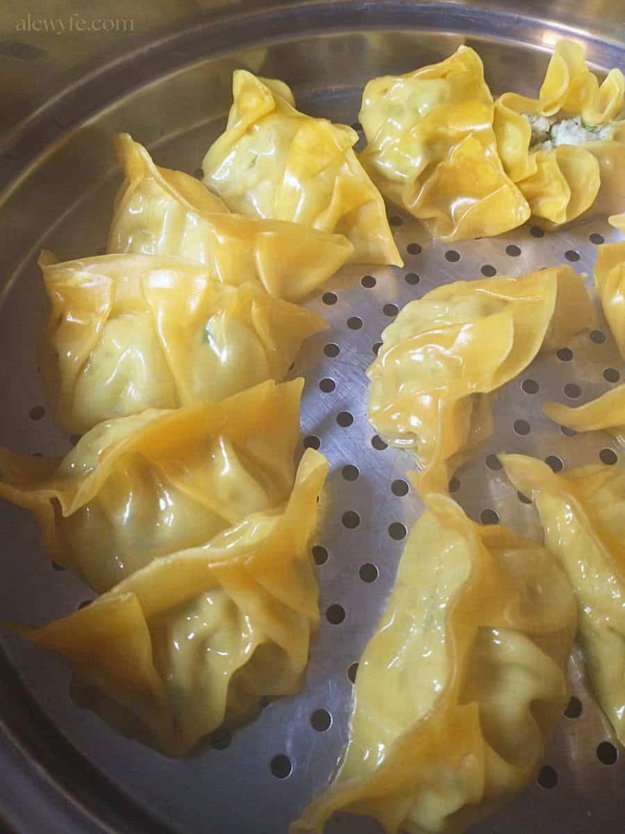 a metal steamer basket full of fish and green onion dumplings.
