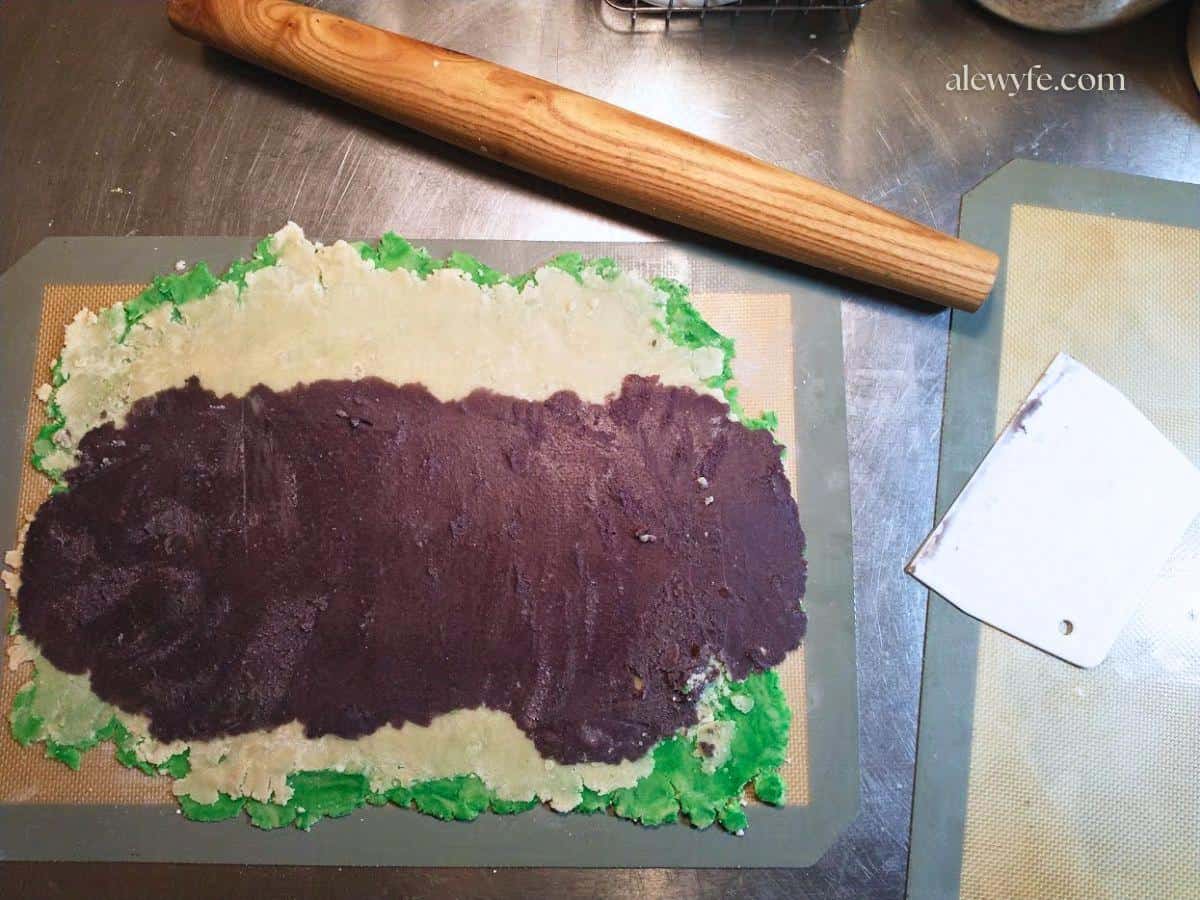 rolling tri-color pinwheel cookie dough on a non-stick baking mat.