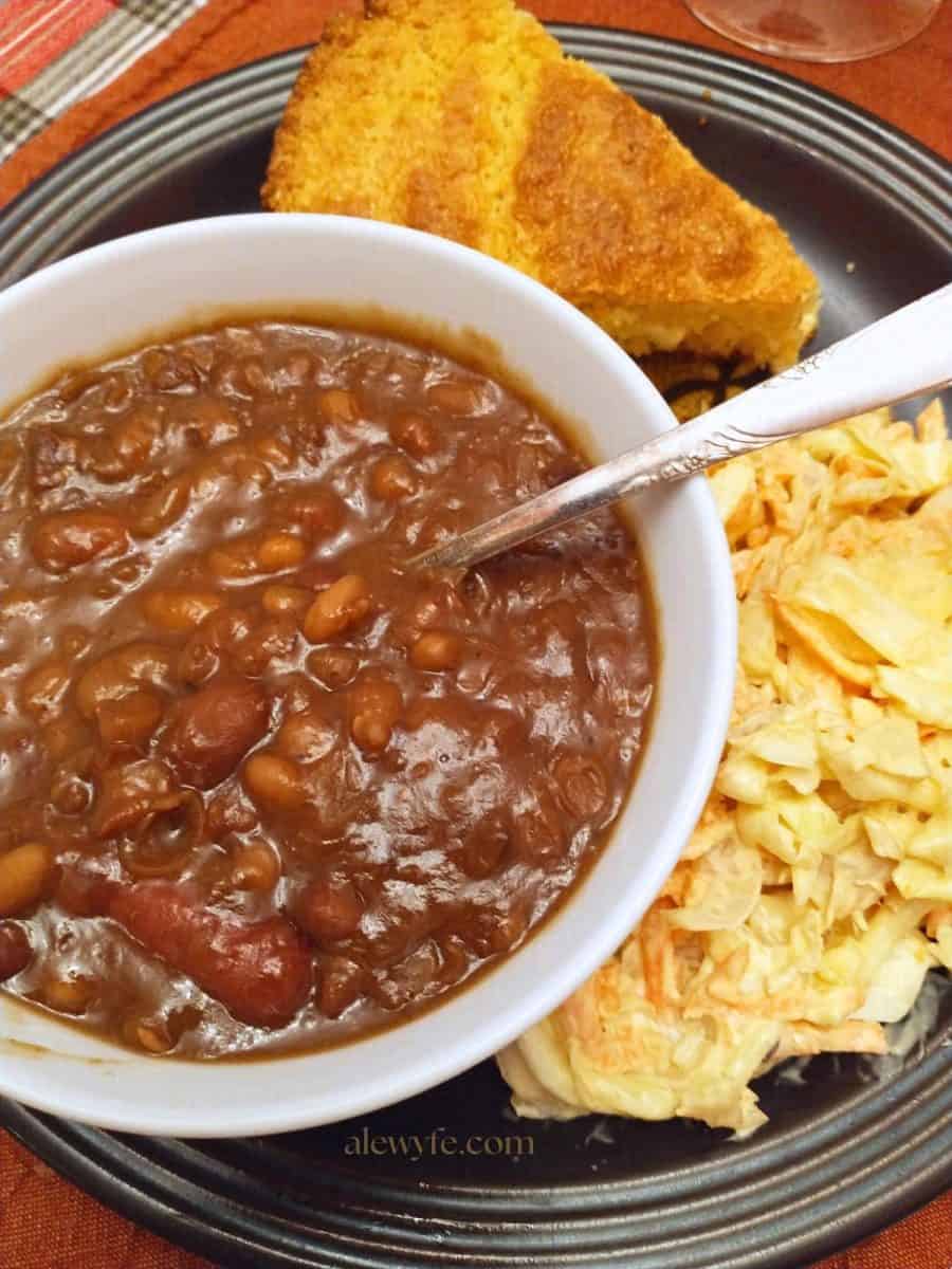a bowl of beans with smoked sausages, creamy coleslaw, and cornbread.