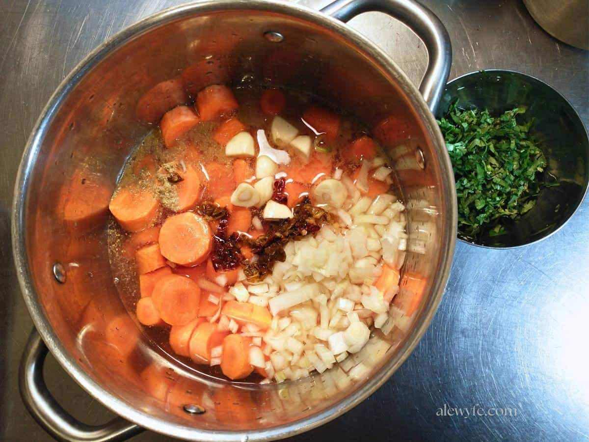 a saucepan with chopped carrots, onions, garlic, habaneros, and seasonings, with a bowl of green cilantro next to it.