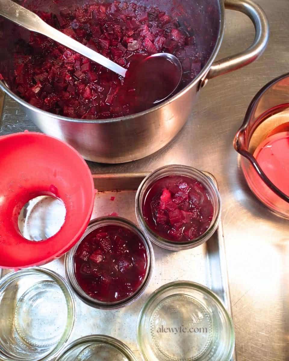 A pot of horseradish beet relish being ladled into canning jars with a wide-mouth funnel.