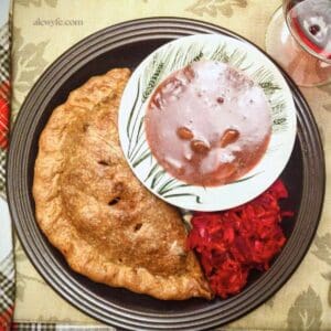 Close-up top-down photo of venison pasty dinner plate with dish of mushroom gravy and a side of red sauerkraut.