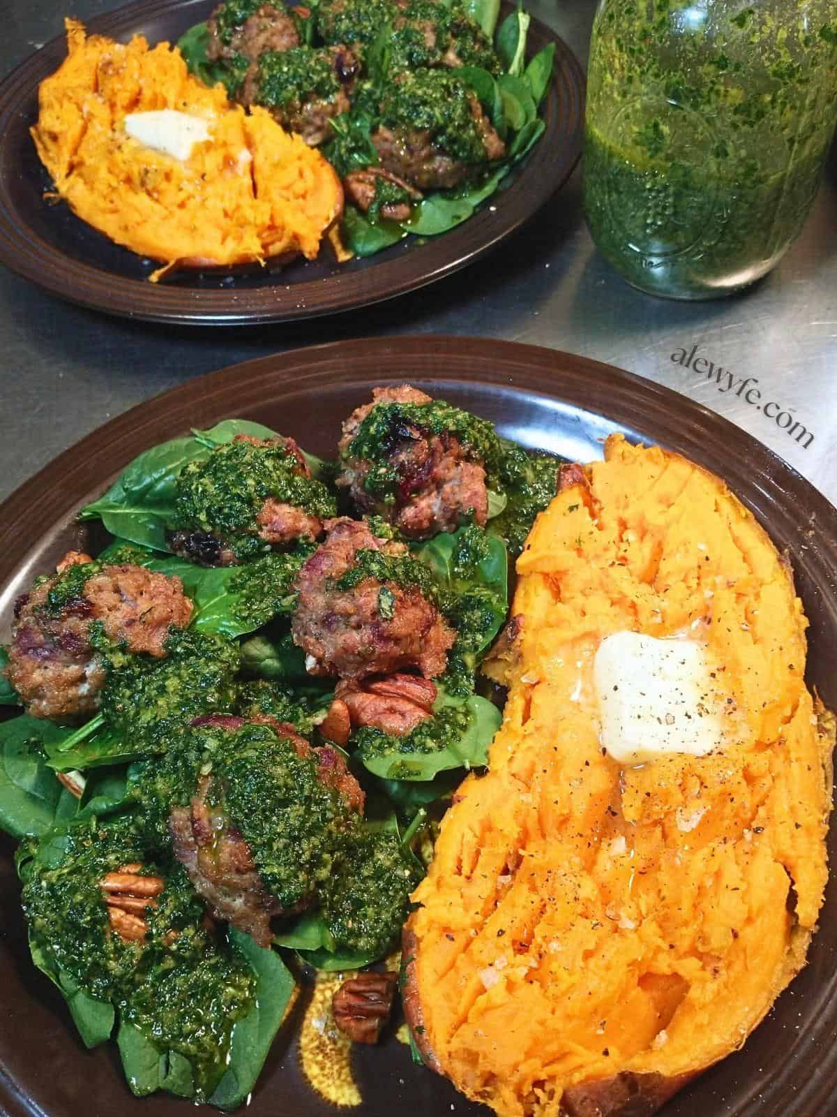 two plates with turkey meatballs served on a bed of salad, with herb pesto and baked sweet potatoes.