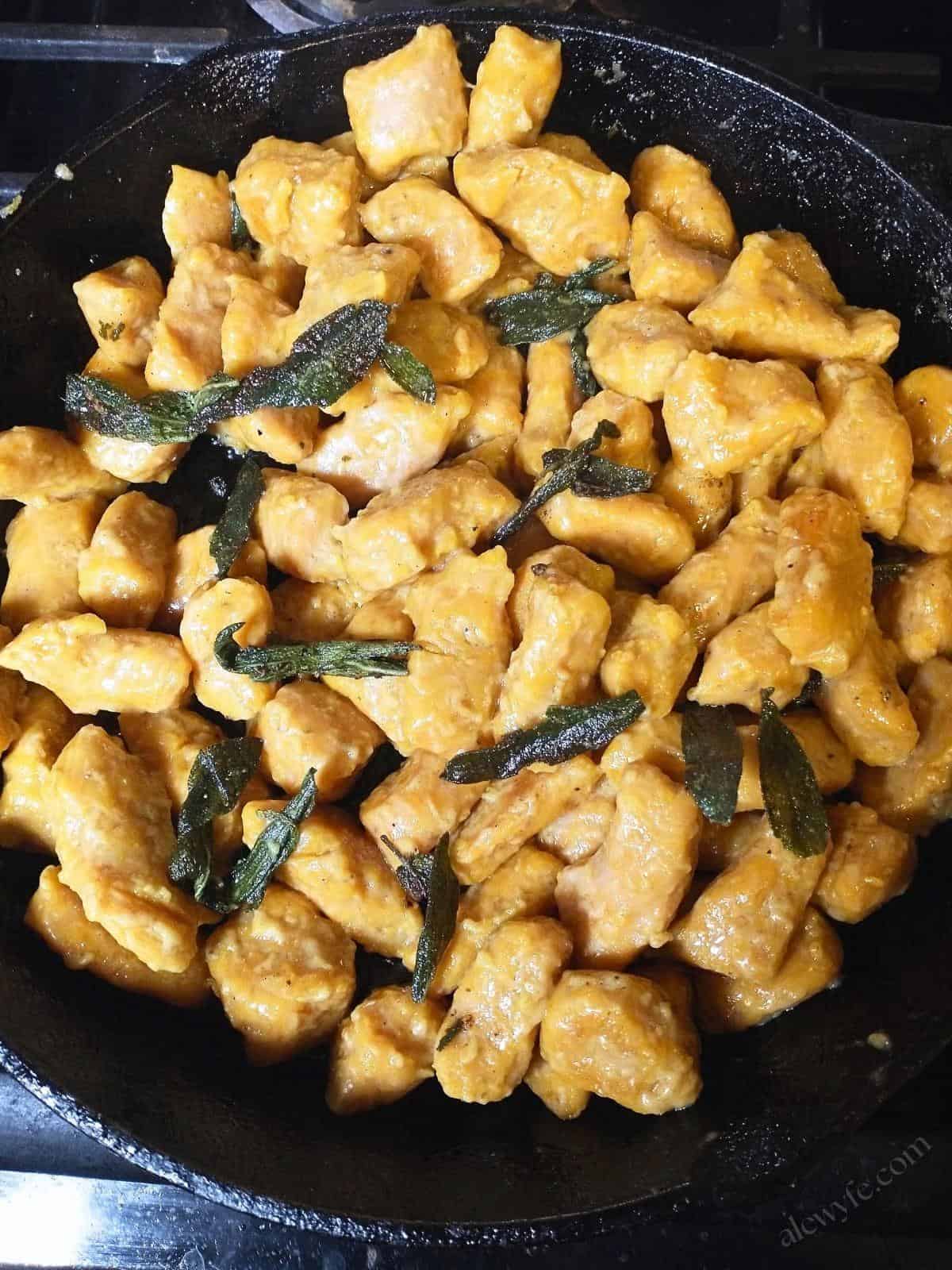 a cast iron skillet with bright orange pumpkin gnocchi and fried sage leaves.
