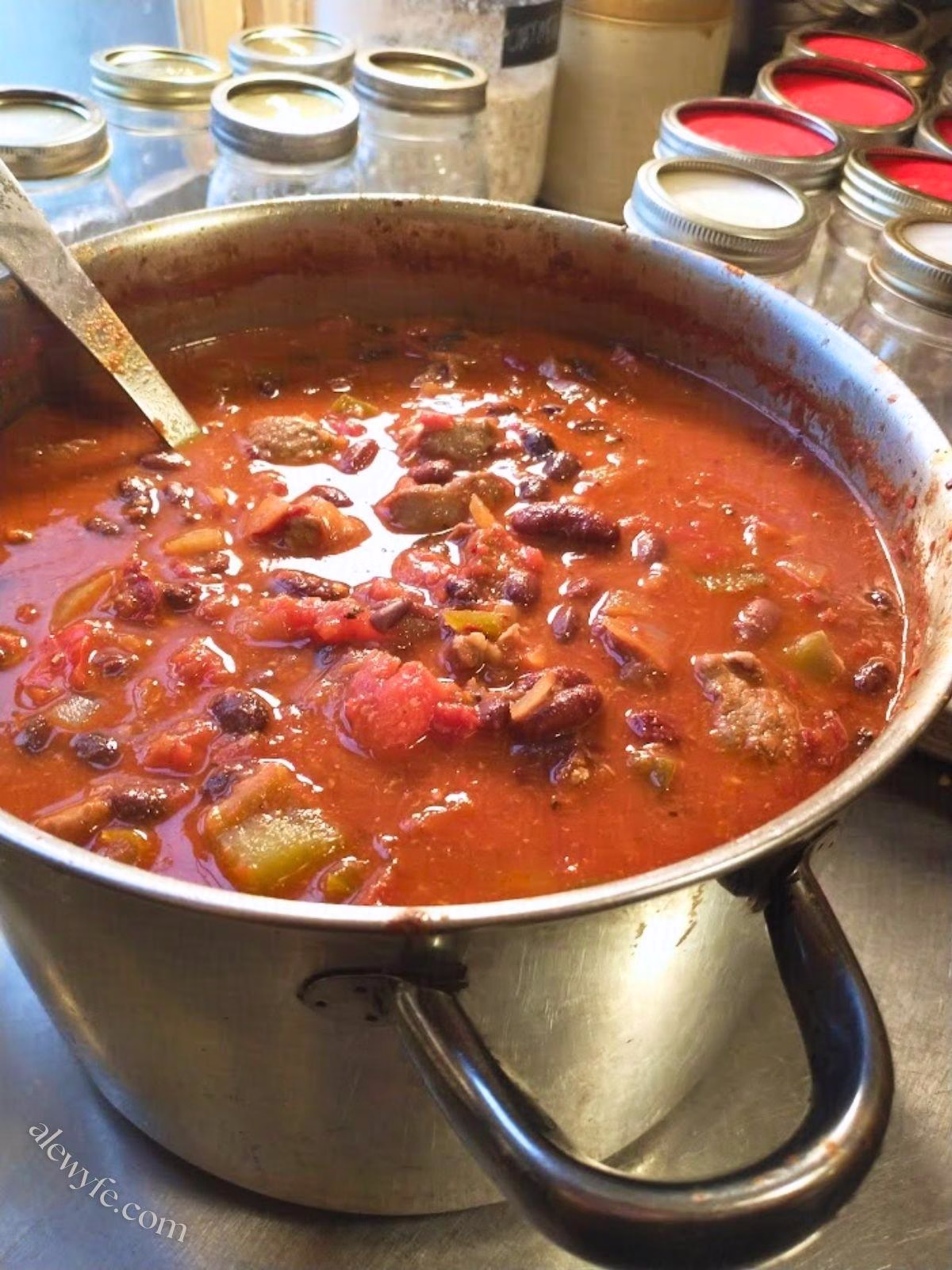 large pot of chipotle venison steak and bean chili ready to fill the canning jars in the background.