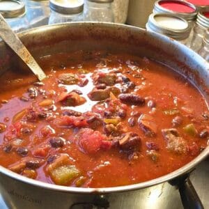 close up photo of a pot of chipotle steak and bean chili ready to can, with canning jars in the background.
