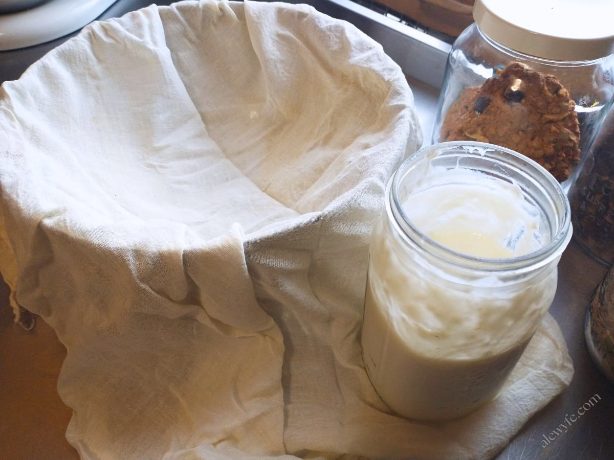 a bowl lined with cheesecloth next to a jar of plain homemade yogurt.
