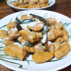 close-up photo of a plate of homemade pumpkin gnocchi with fried sage leaves and Parmesan cheese.