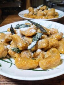 two plates of pumpkin gnocchi with fried sage leaves and Parmesan cheese on top.