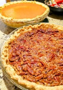 two deep dish pies are cooling on a granite countertop, one pecan, and one pumpkin. A dish of candy is in the background.