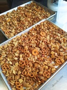 two half-sheet baking trays of smoky old bay flavored homemade chex mix cooling on a stainless table. alewyfe.com watermark.