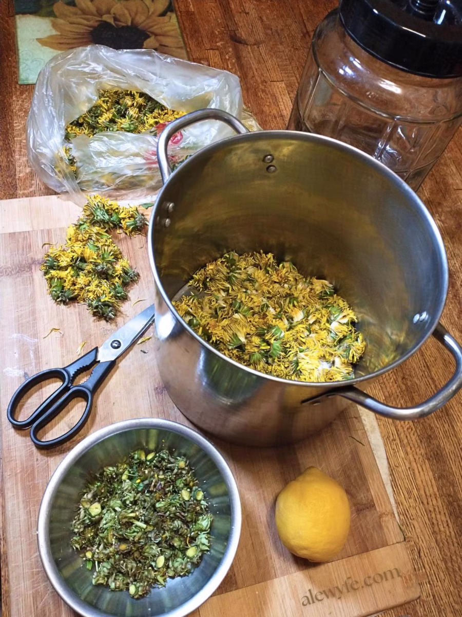 a cutting board with whole dandelion flowers in a bag, a bowl of green flower calyxes, a whole lemon, and mostly yellow flower petals in a pot.