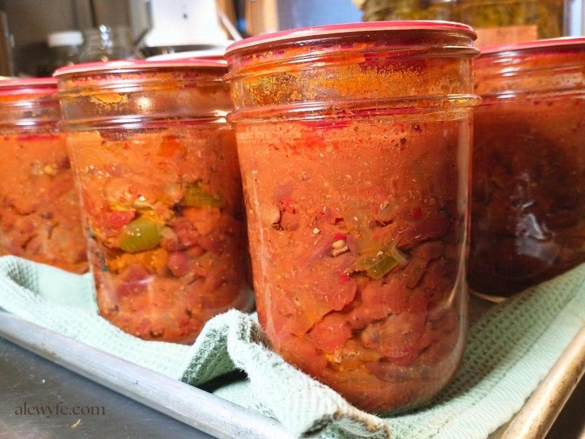 a tray with jars of steak and bean chili on a tea towel, just after washing the jars and removing the canning rings.